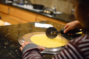 Big Brother using a pizza cutter to make Indian food